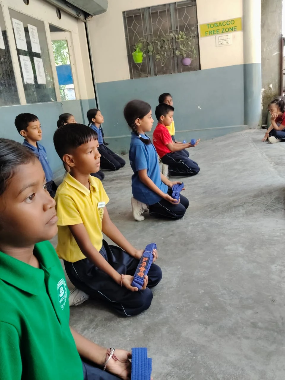 Students kneeling proudly with their earned blue belts during martial arts ceremony