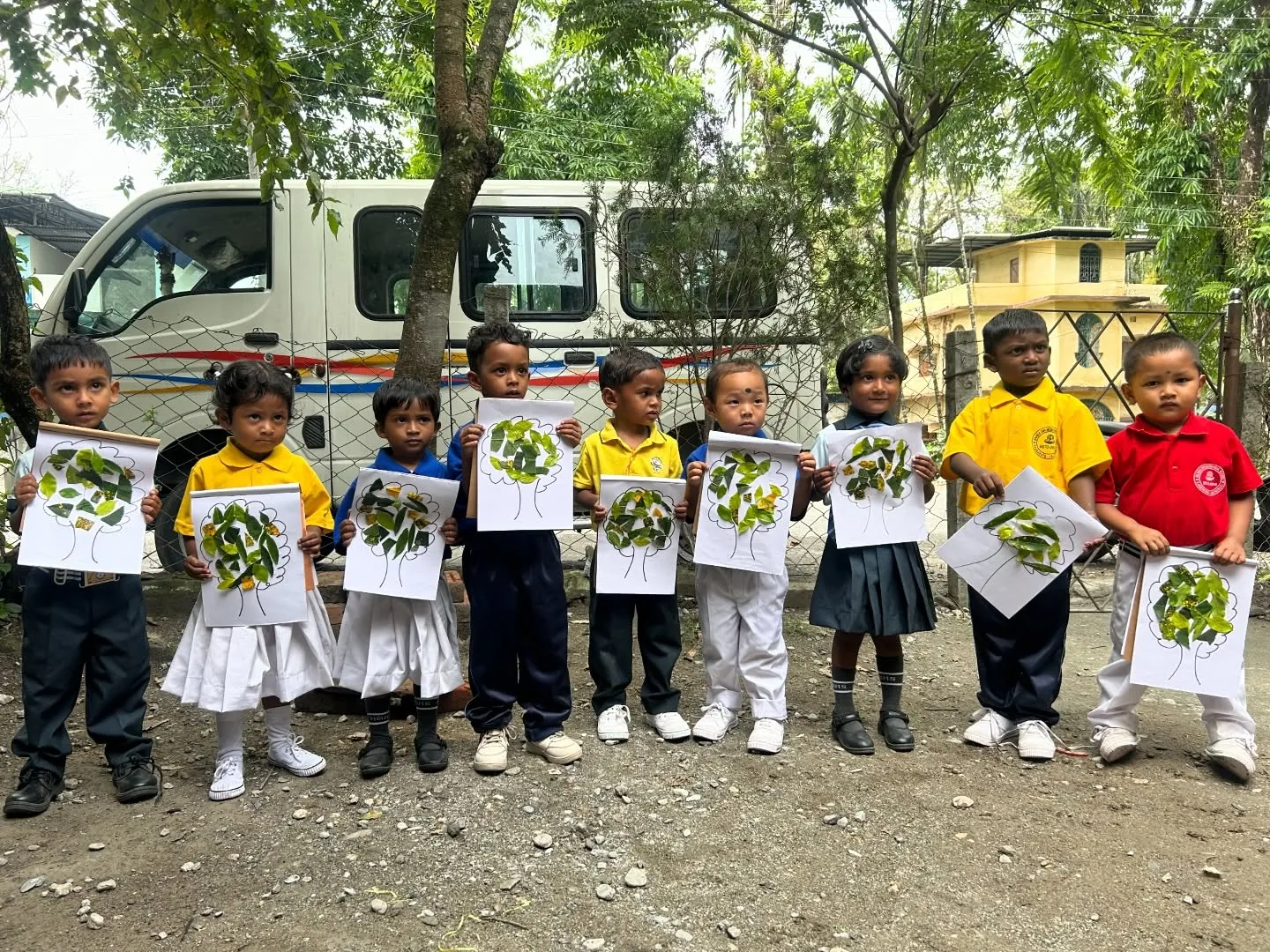 Young children holding up leaves arranged on tree drawings